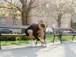 Adult man tying shoes on park bench in morning sunlight, ready for jogging.