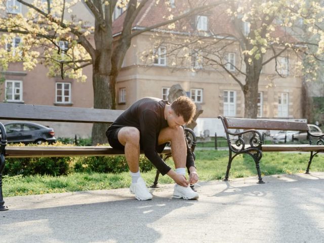 Adult man tying shoes on park bench in morning sunlight, ready for jogging.